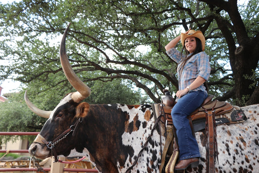 a woman riding on the back of a brown and white cow