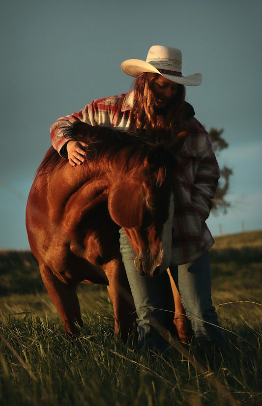 Cowboy hugging his horse in a field.