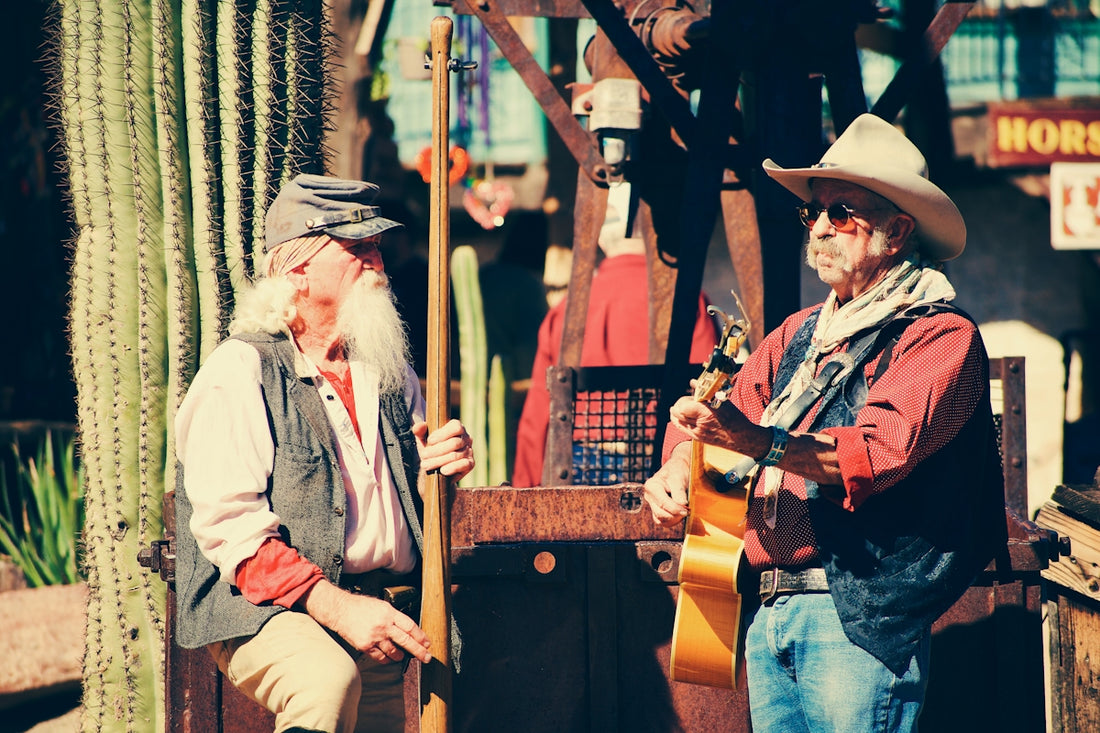 Two cowboys playing music outdoors with cacti.