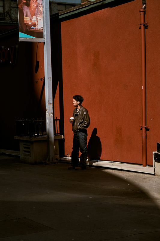 Man with coffee cup stands against red wall